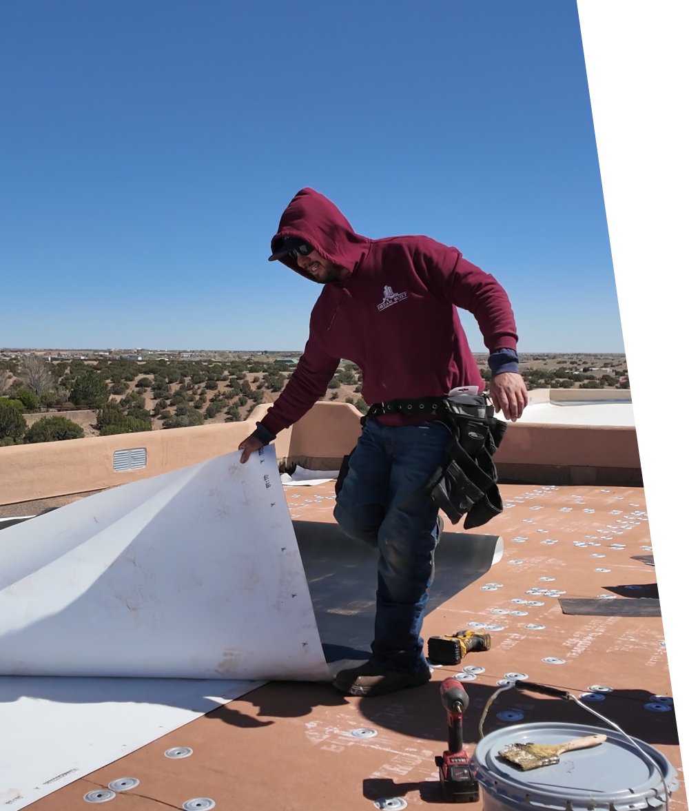 Professional roofing contractor of a top construction company installing a white TPO roof system roll on a flat roof commercial property project in Santa Fe New Mexico.